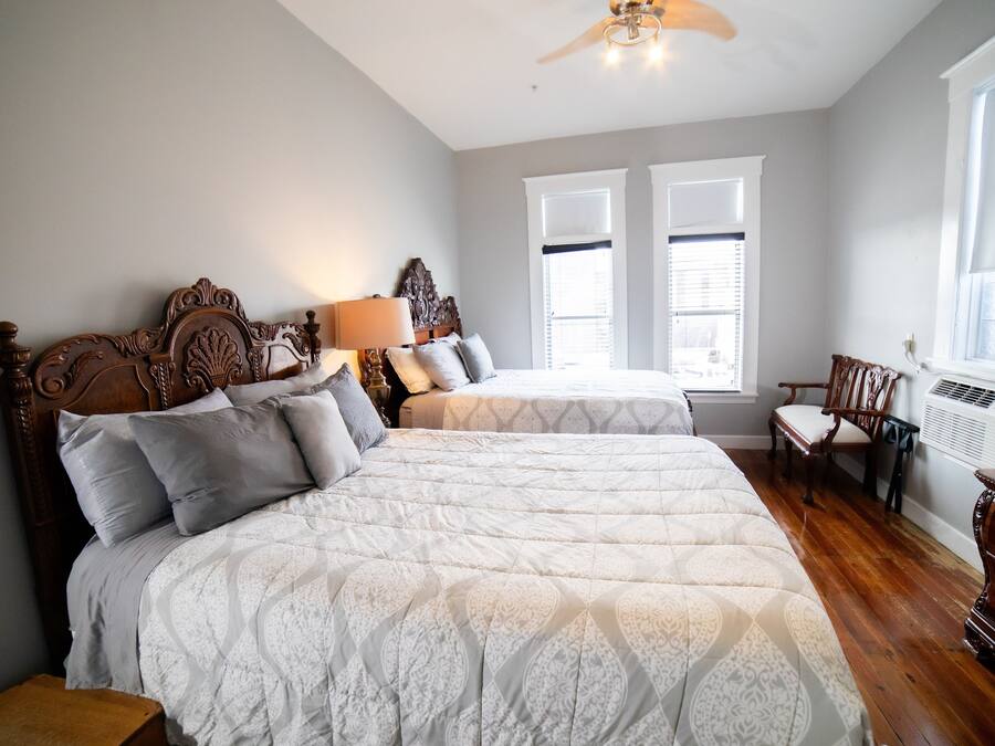 A bedroom with two beds, a wooden headboard, a nightstand, a chair, and a window with blinds.