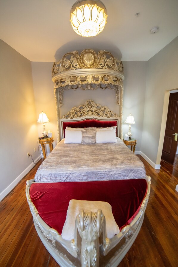 A large bed with an ornate headboard, two bedside tables with lamps, and a chandelier.