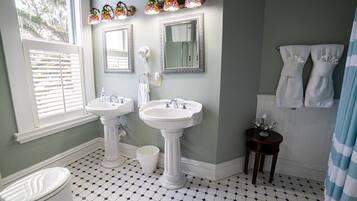 A bathroom with two sinks, a toilet, a window with blinds, a shower curtain, and a tiled floor.