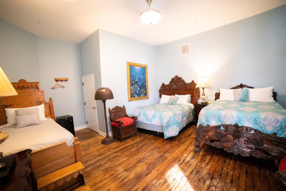 Ein Schlafzimmer mit zwei Betten, Holzboden, einer Tür, einer Wandleuchte und einem gerahmten Bild.