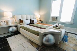 A modern bedroom with a unique bed design, two bedside tables, a nightstand, a window, and a view of the outdoors.