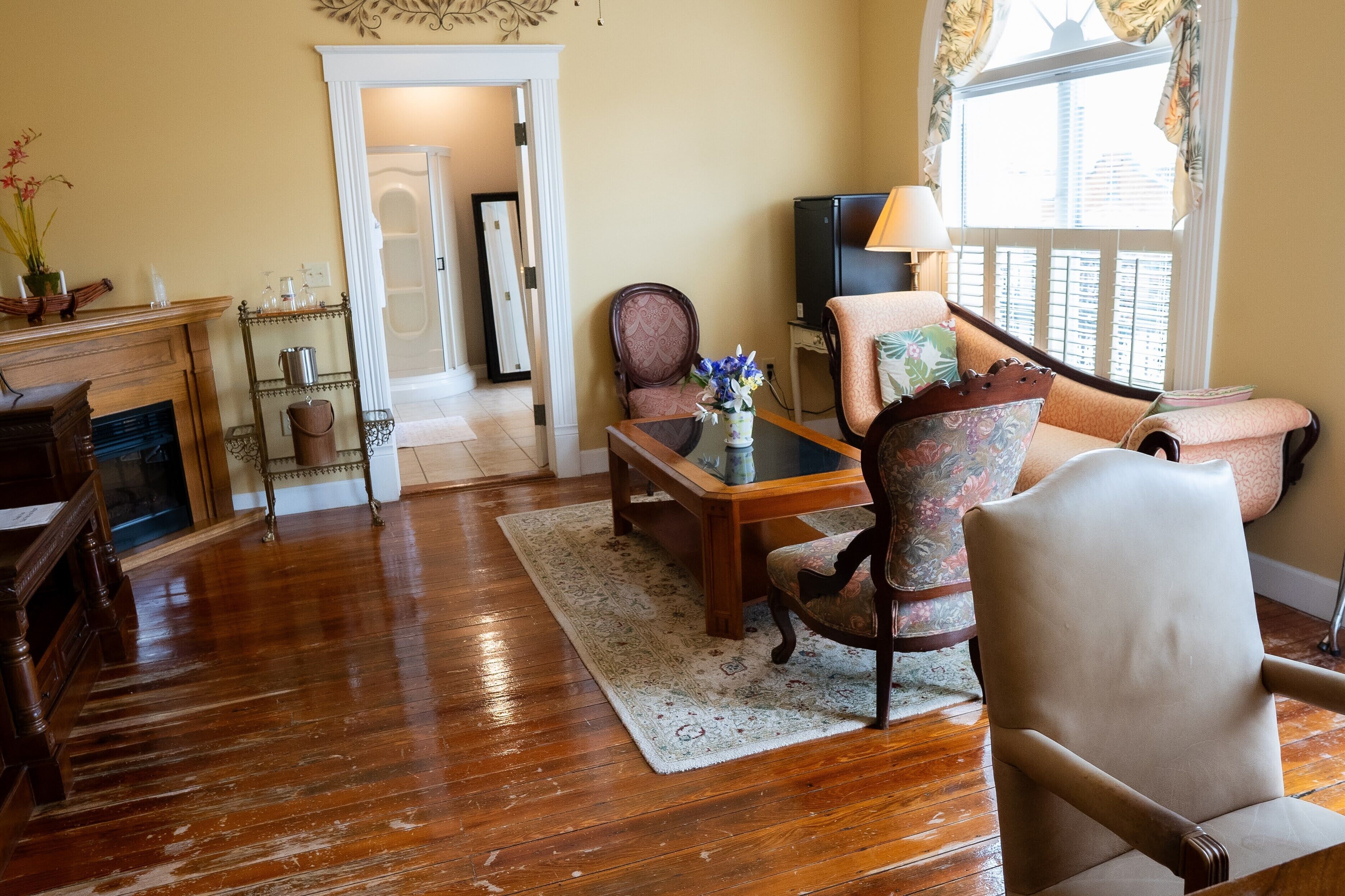 A living room with a wooden floor, a fireplace, a dining table with chairs, a television, and a window with curtains.
