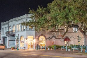 A historic hotel with arched windows and a balcony, surrounded by trees and a decorative fence.