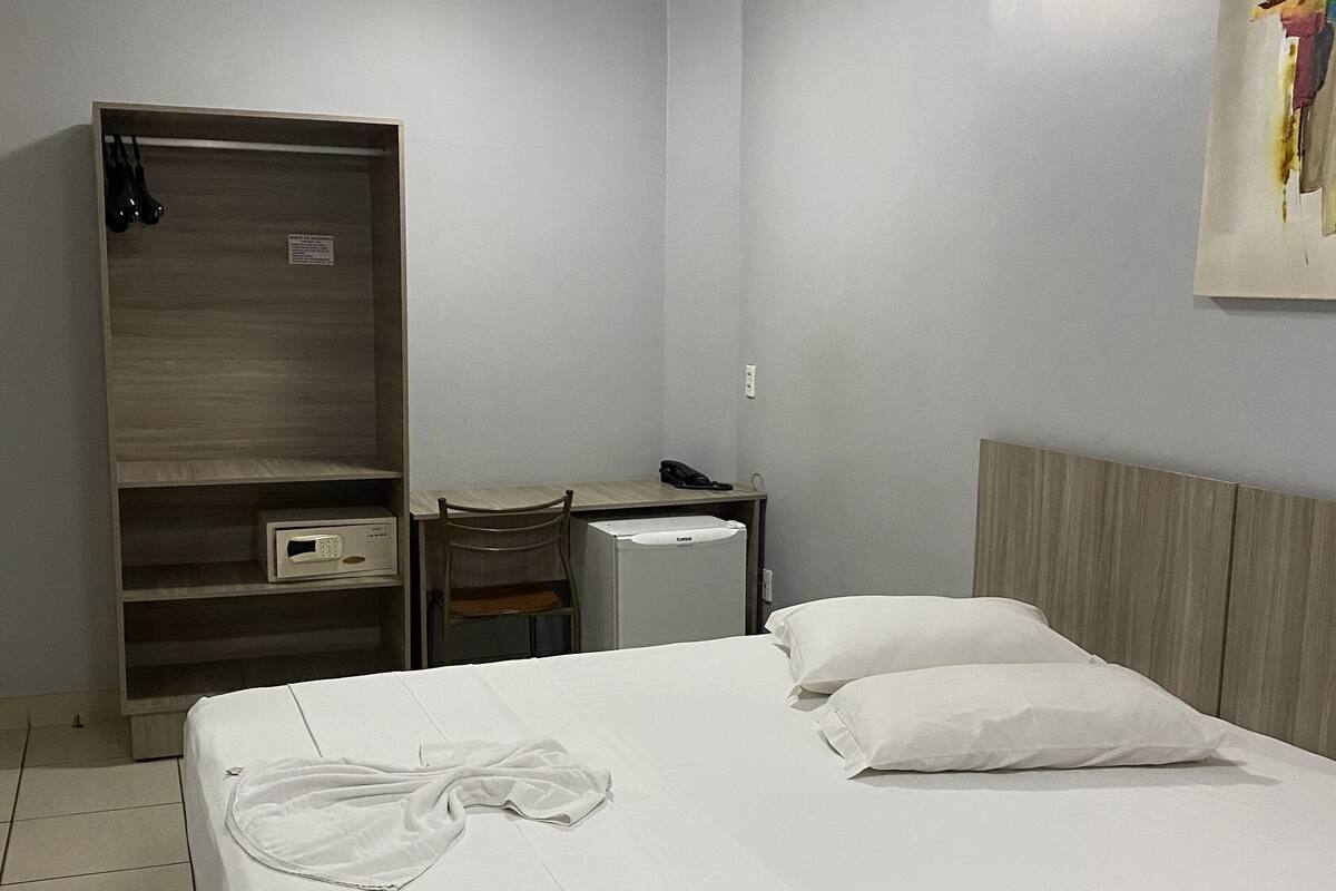 A hotel room with a bed, a desk, a wardrobe, and a small refrigerator.