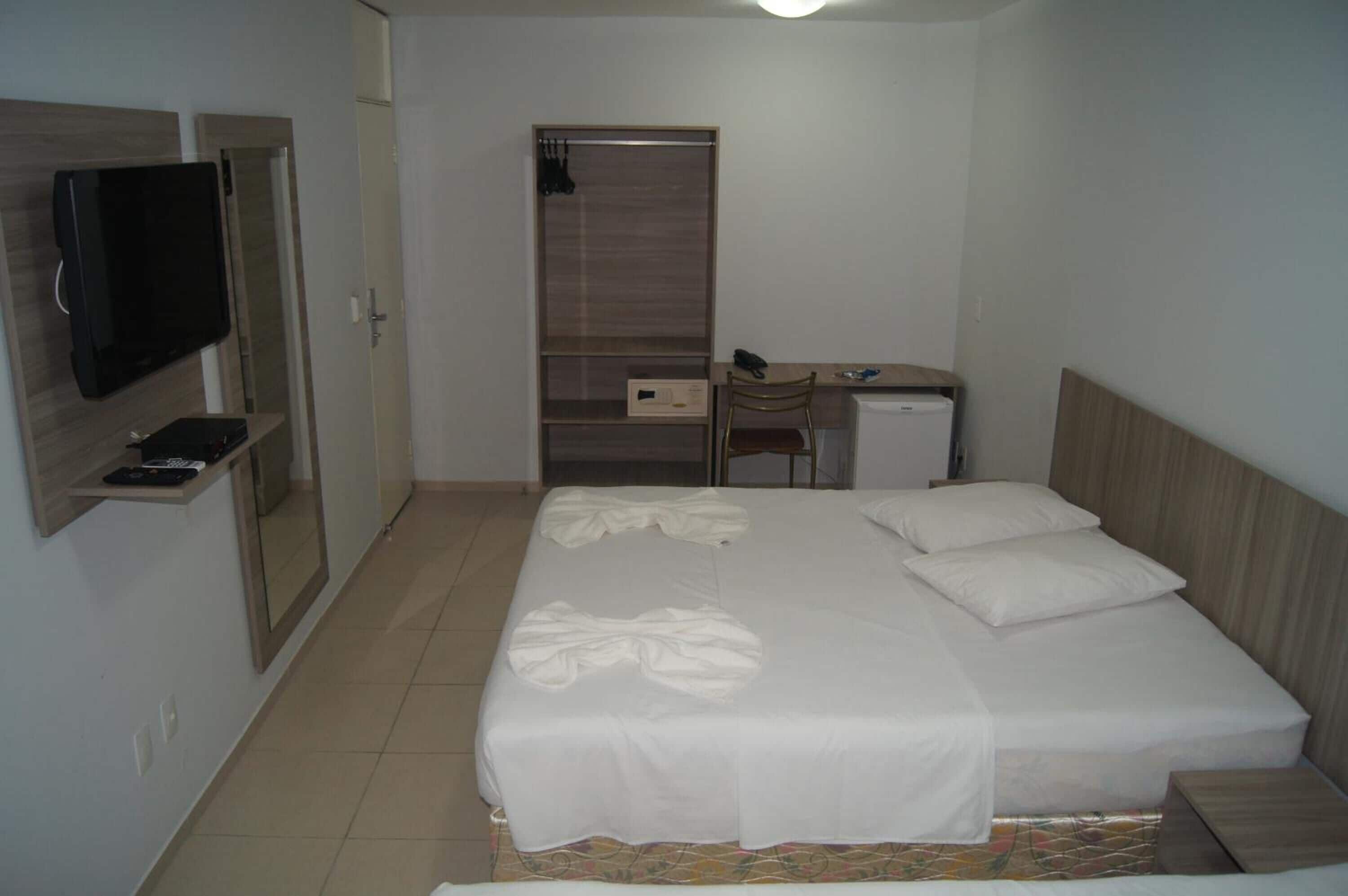 A bedroom with a bed, a desk, a chair, a television, and a wardrobe.