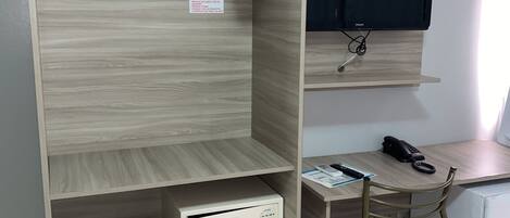 A room with a wooden wardrobe, a desk with a chair, a mounted TV, and a telephone.