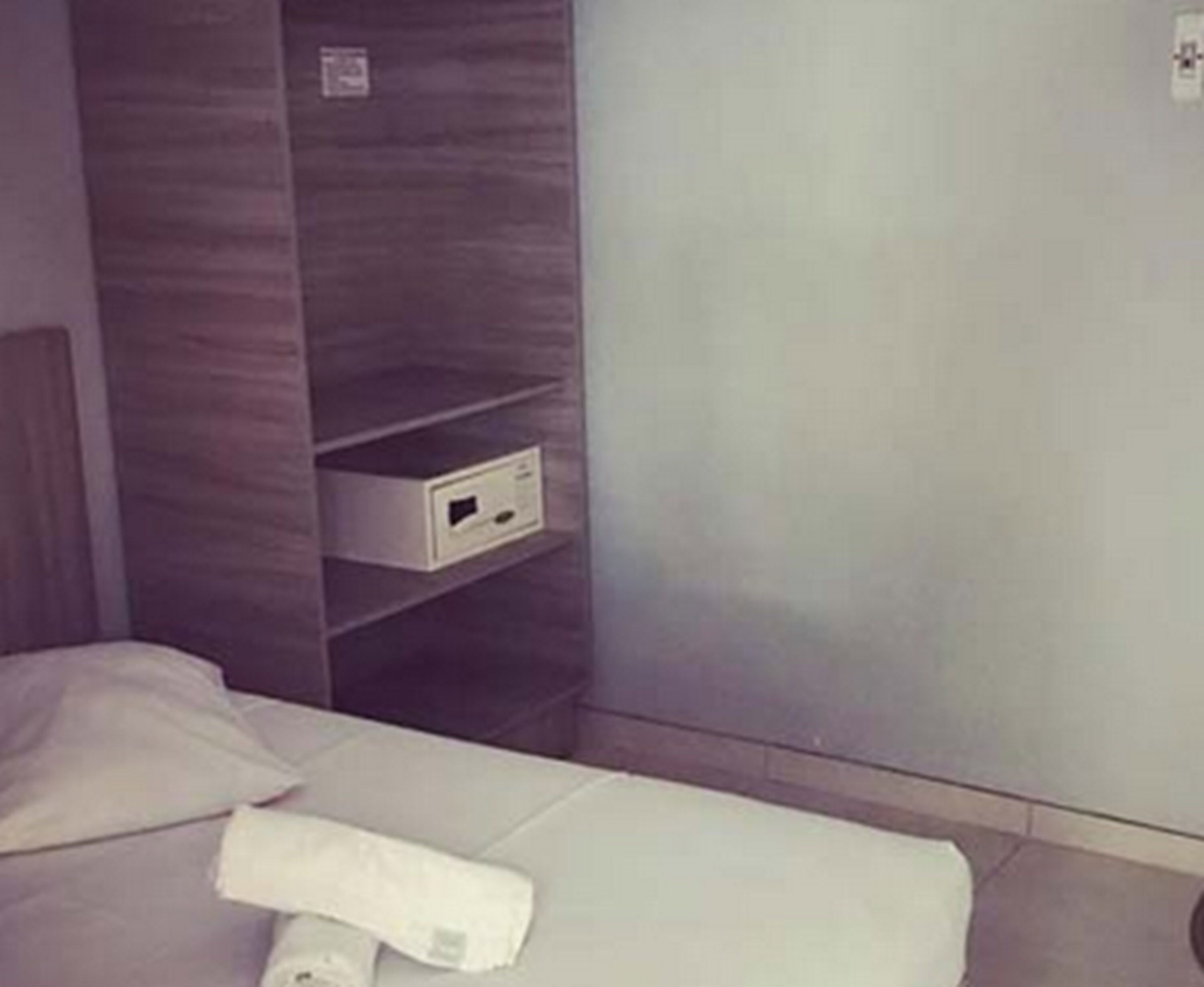 Una habitación de hotel con una cama, una unidad de almacenamiento empotrada y una pared lisa.