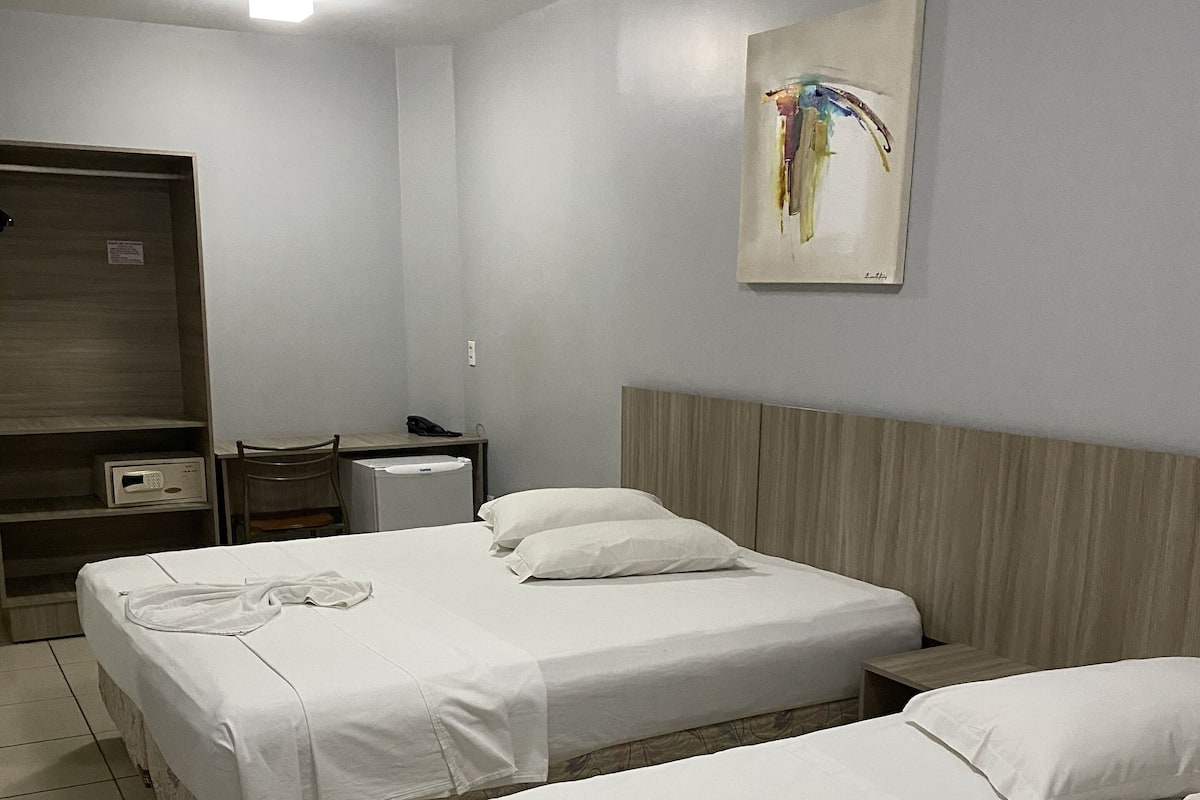 A hotel room with two beds, a desk, a chair, a telephone, and a painting on the wall.