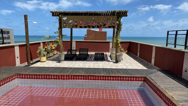 A rooftop terrace with a pergola, lounge chairs, potted plants, and a view of the ocean. - Hotel Fortaleza Inn (Fortaleza)