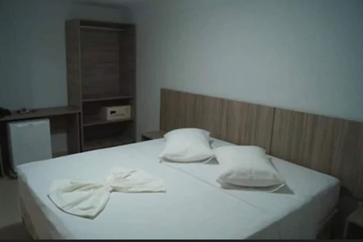 A hotel room with a bed, a wooden headboard, a wardrobe, and a small desk with a lamp.