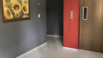 Um corredor com chão ladrilhado, um quadro de girassóis na parede, uma parede vermelha e uma porta de madeira.