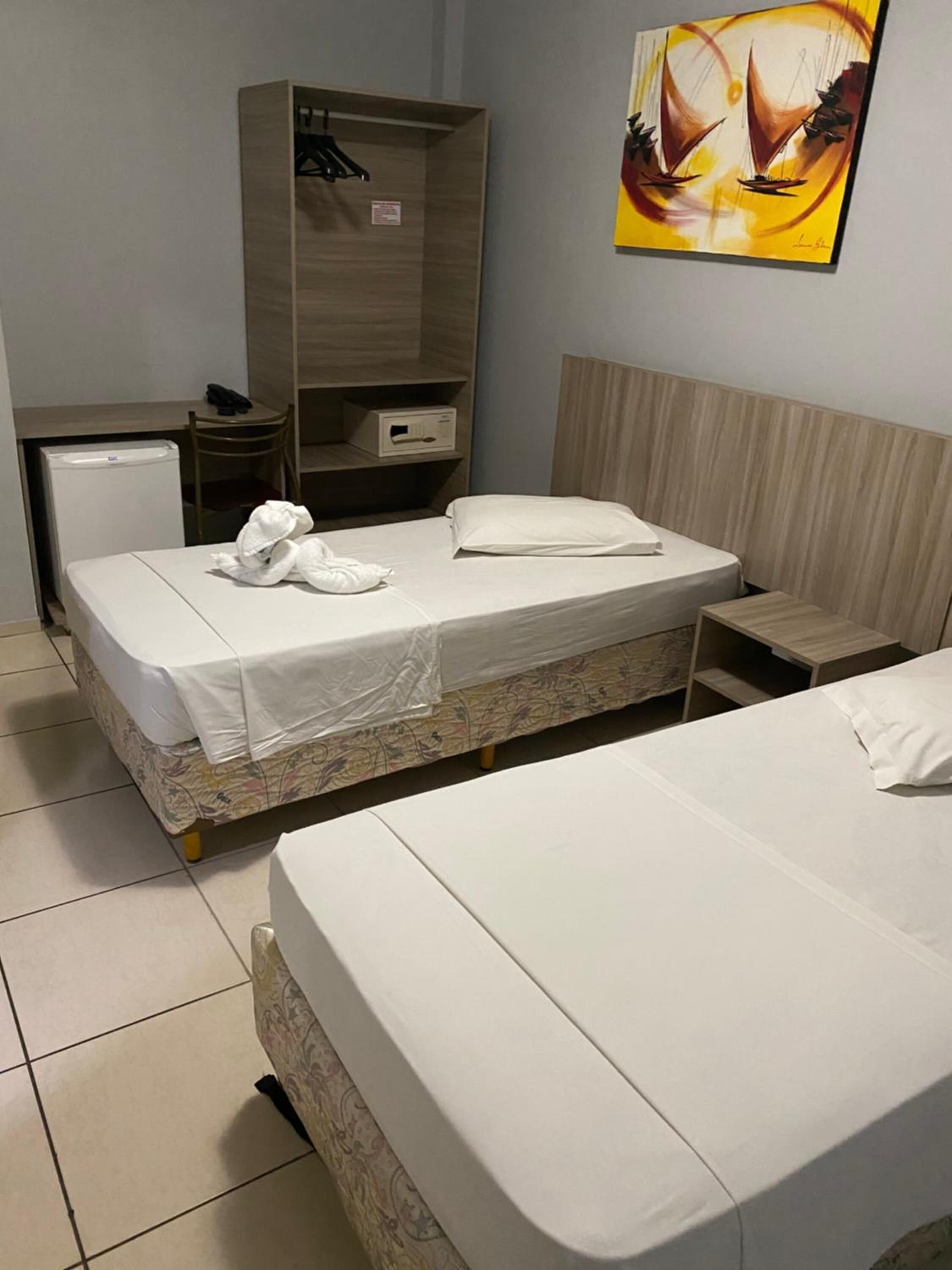 A hotel room with two beds, a wardrobe, a desk, and a small refrigerator.