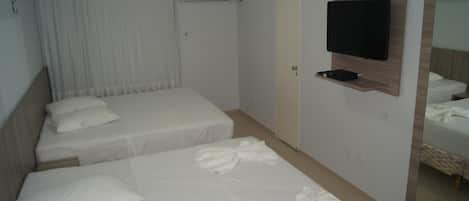 A hotel room with two single beds, a flat-screen TV mounted on the wall, a door, and a mirror reflecting part of the room.