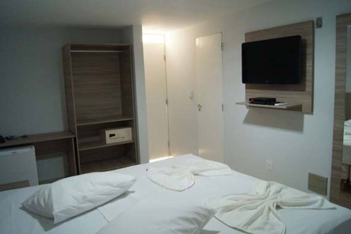 A bedroom with a bed, a wardrobe, a television mounted on the wall, and a desk with a computer.