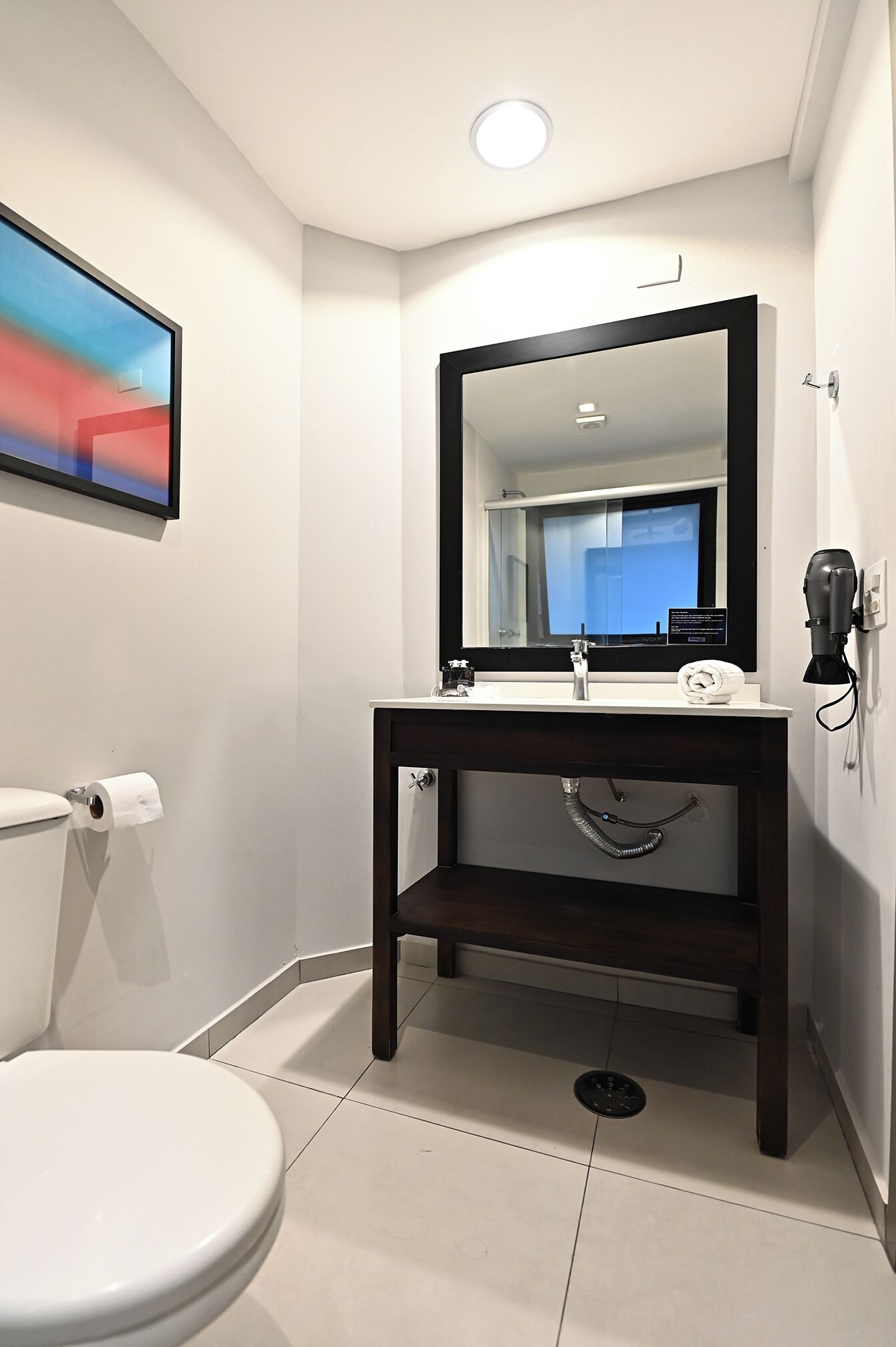 Une salle de bain moderne avec des toilettes blanches, un meuble-lavabo en bois foncé, un grand miroir et une douche.