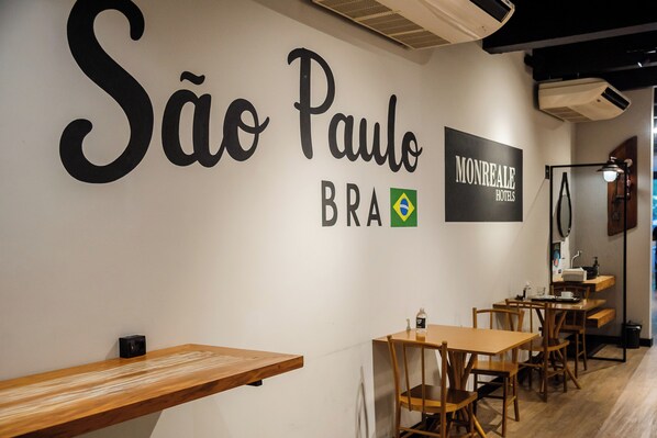 A restaurant interior with a wall sign reading "SÃO PAULO BRAZIL" and "MONREALE HOTELS". There are wooden tables and chairs.