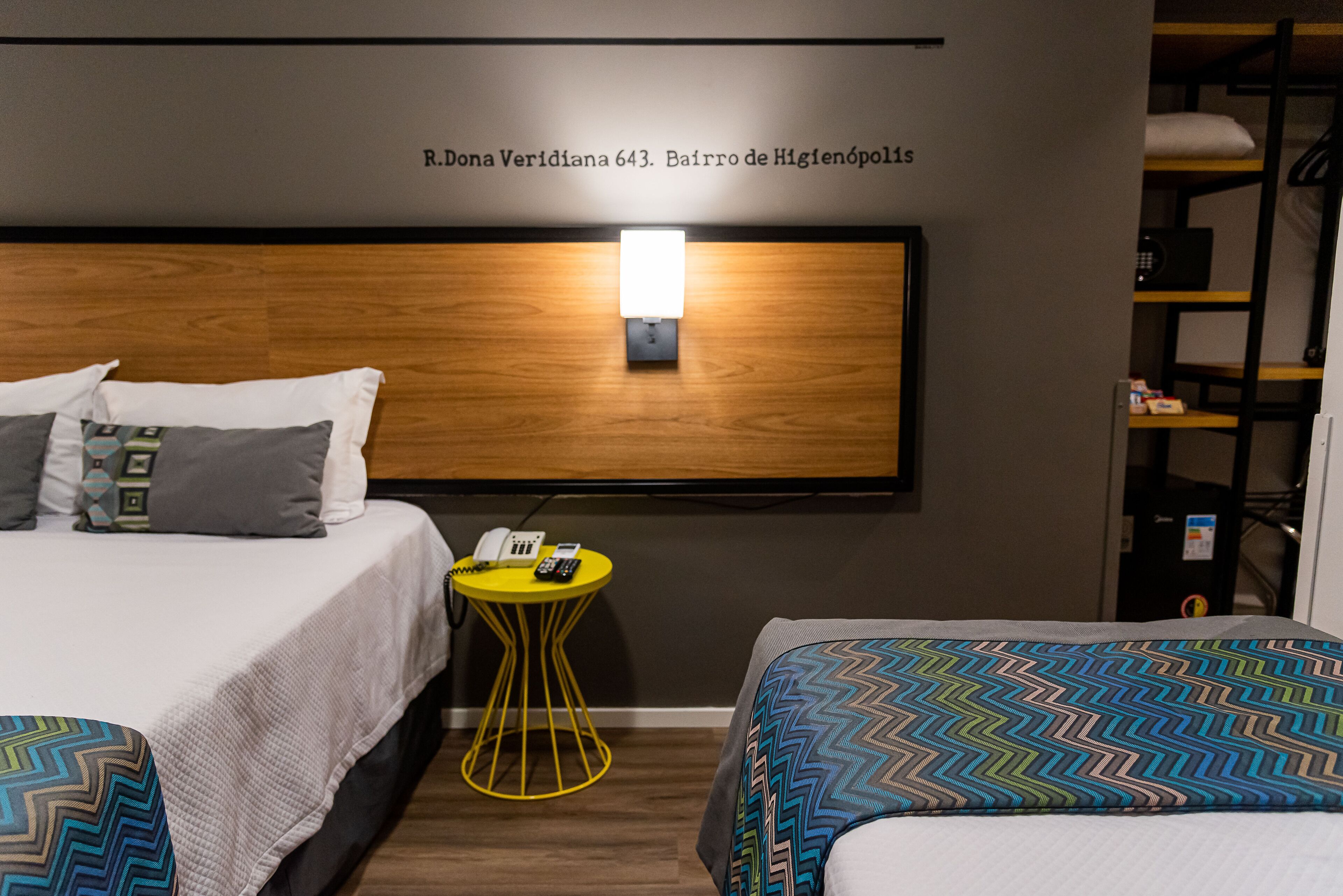 A hotel room with a wooden headboard, a bedside table with a phone and a lamp, and two beds with patterned bedding.