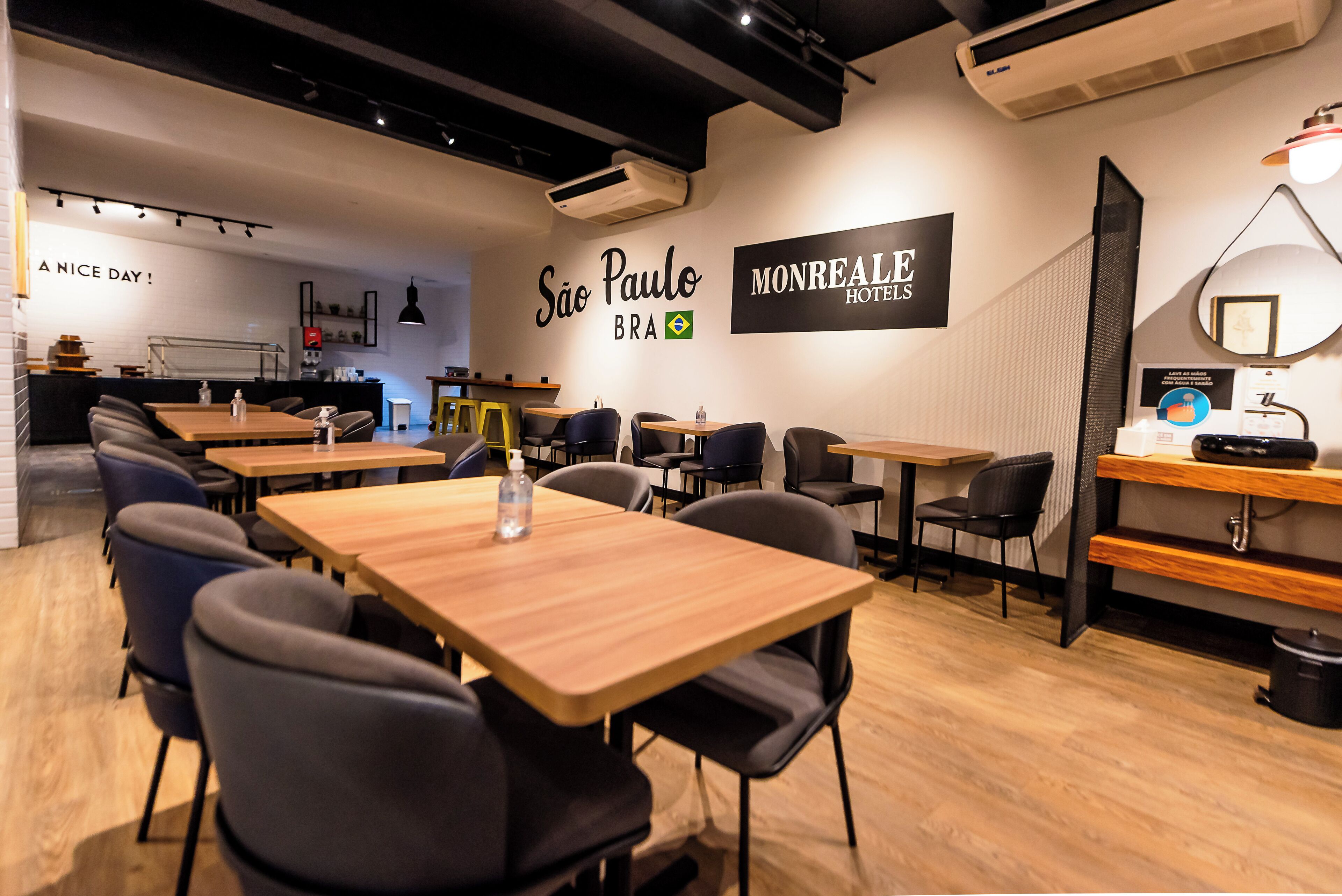 Un interior moderno de hotel con varias mesas y sillas para comer, una zona de cocina y una pared con el nombre y el logotipo del hotel.
