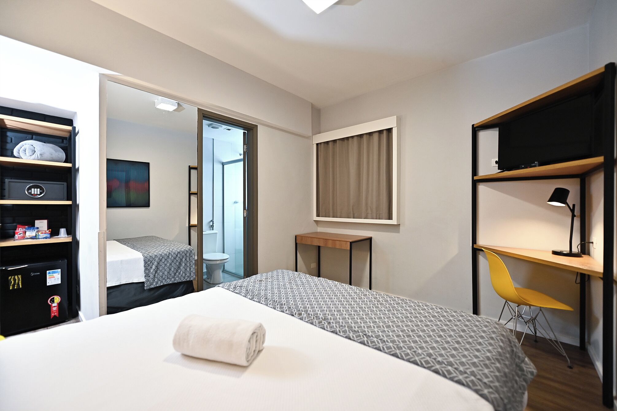 A hotel room with a bed, a desk, a TV, a wardrobe, and a bathroom visible through an open door.
