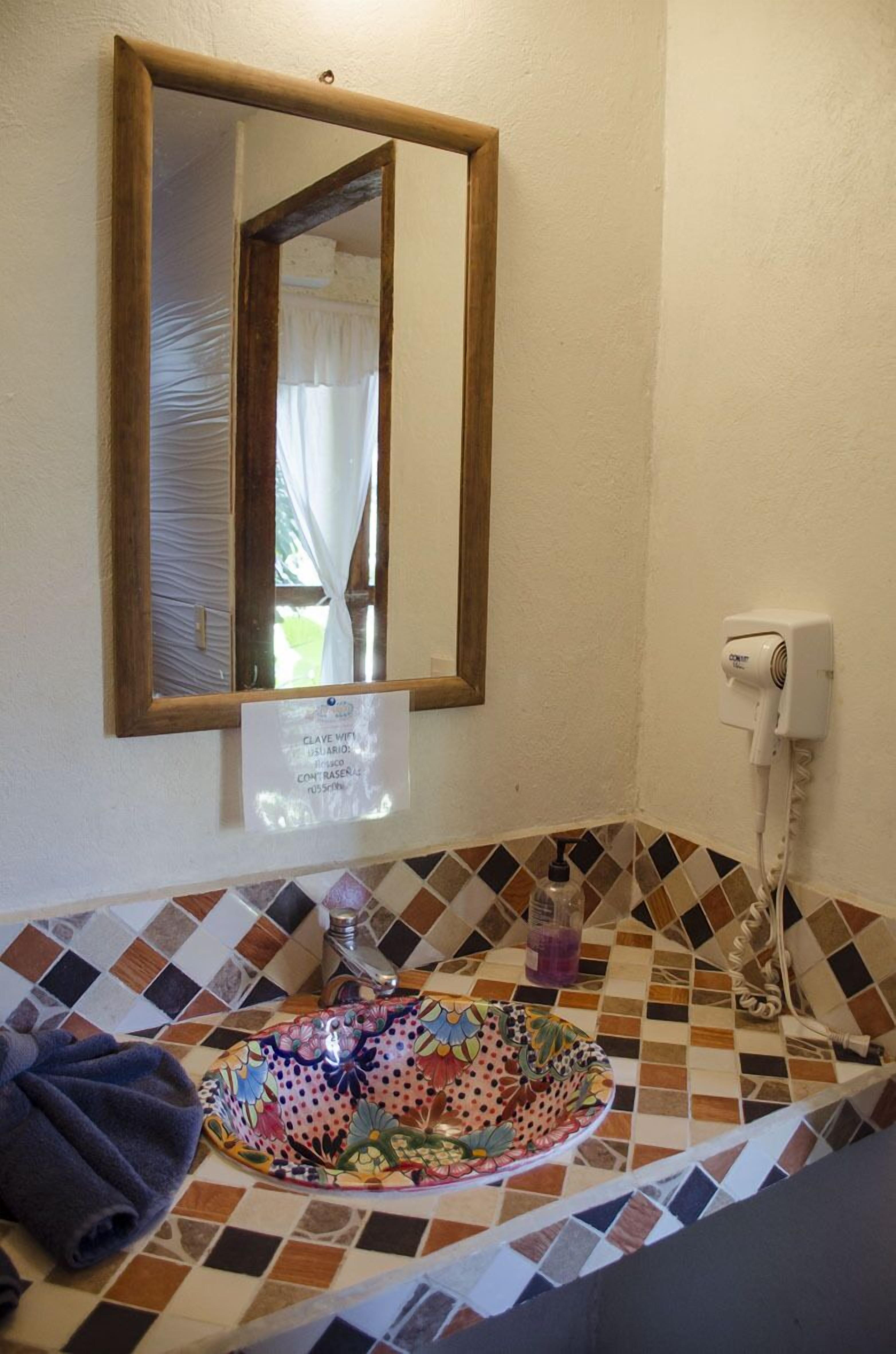 Un baño con lavamanos de azulejos, un espejo y un secador de pelo en la pared.