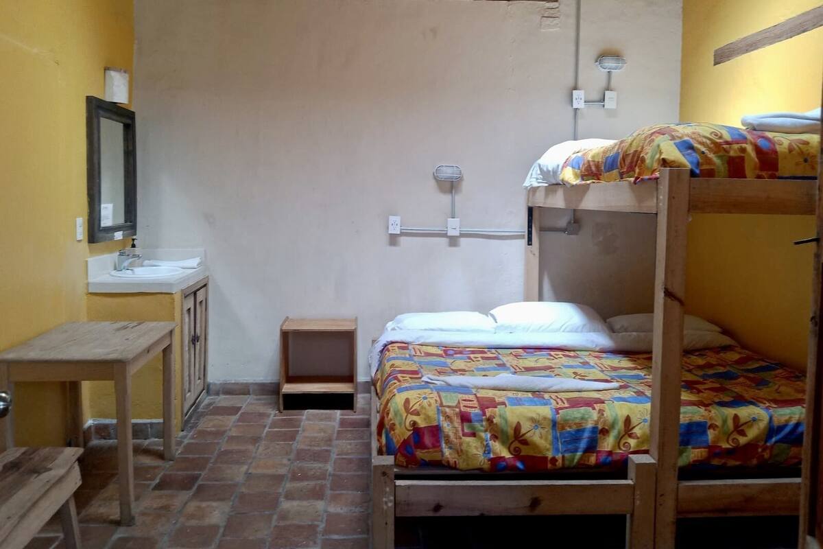 Une chambre de dortoir avec des lits superposés, une petite table en bois, un lavabo et un miroir.