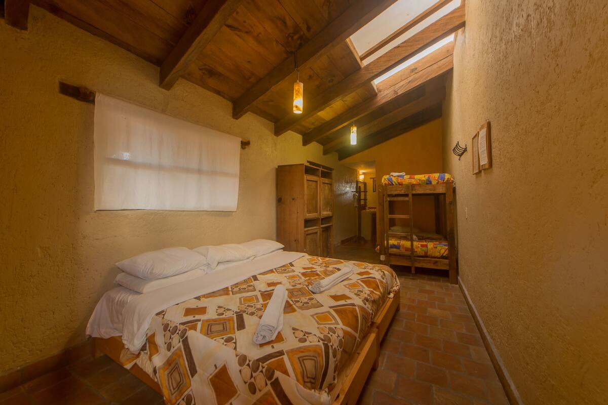 Une chambre à coucher avec un lit, une fenêtre avec des stores, un plafond en bois et un plancher en briques.
