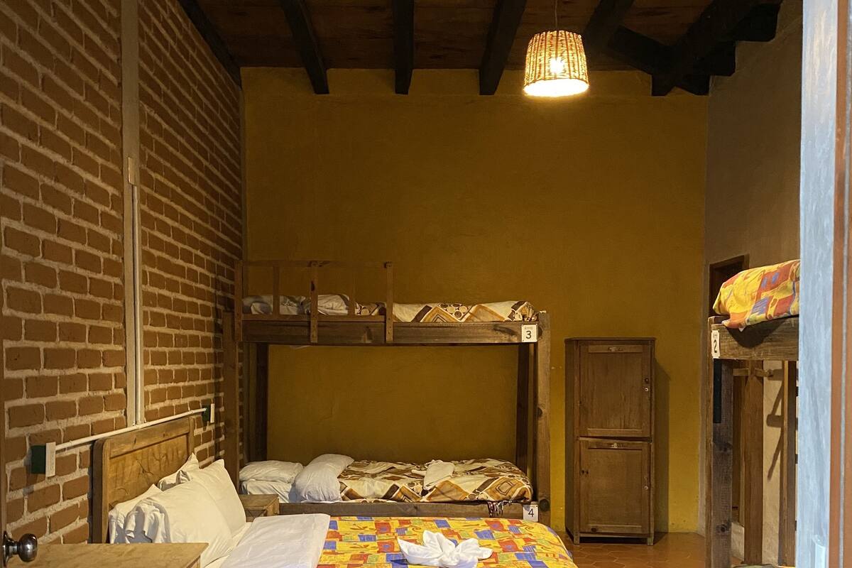 Une chambre de dortoir avec des lits superposés, un bureau en bois, un banc et un sol carrelé.
