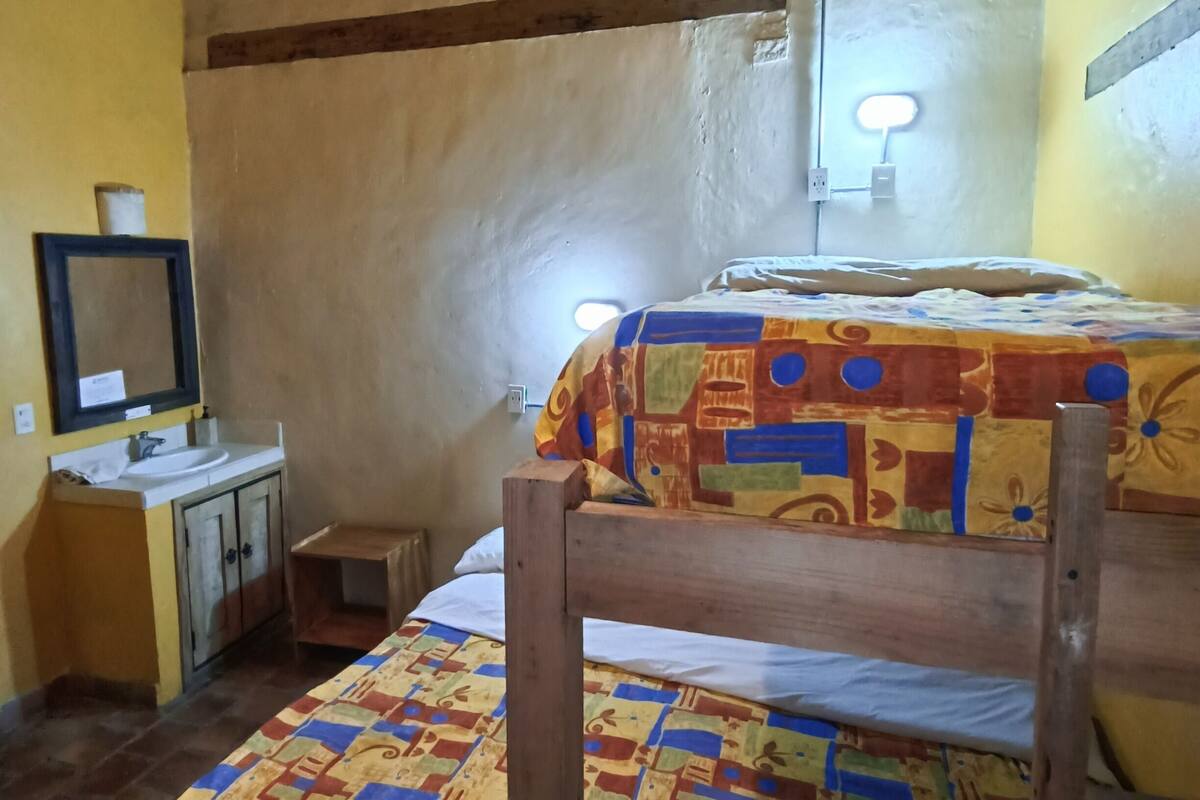 Une chambre de dortoir équipée de deux lits superposés, d’un petit bureau avec un miroir, d’un lavabo et d’une lampe fixée au mur.