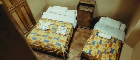 Dos camas con colchas estampadas y ropa de cama blanca, una mesita de noche de madera y un suelo de baldosas.