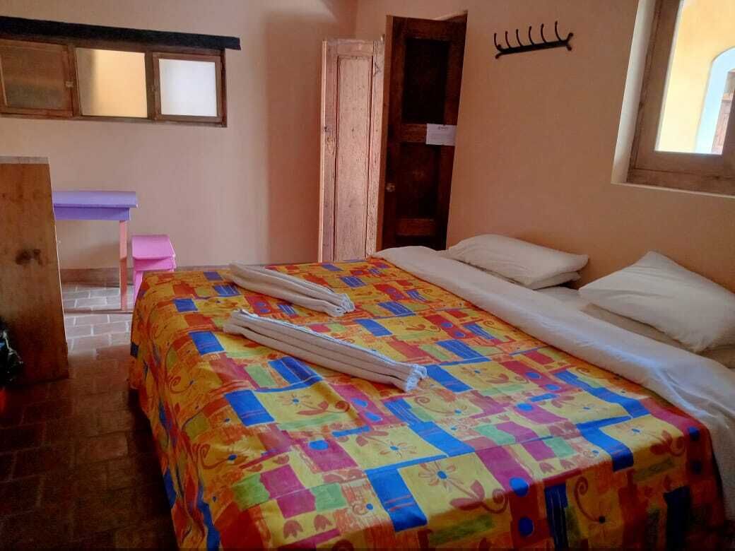 A room with a bed, a wooden door, a small table, and a window.