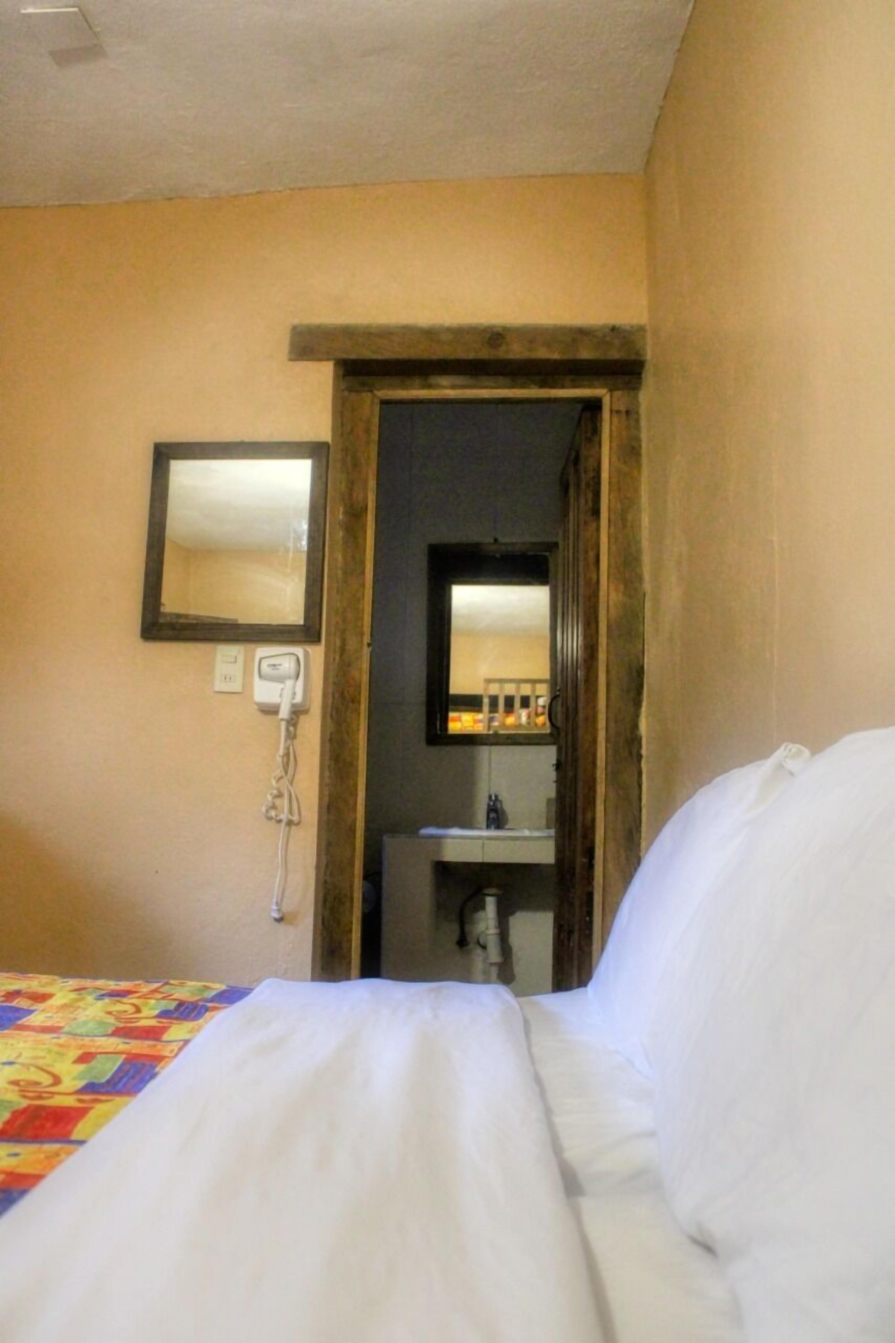 A hotel room with a bed, a mirror, a sink, and a door leading to another room.