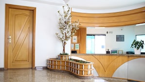 Un área de recepción con un mostrador de madera, una planta en maceta y una zona de atención al cliente.