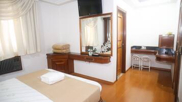 A hotel room with a bed, a vanity with a mirror, a desk, and a chair.