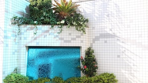 Pared de azulejos con una ventana azulada y plantas verdes creciendo en ella.
