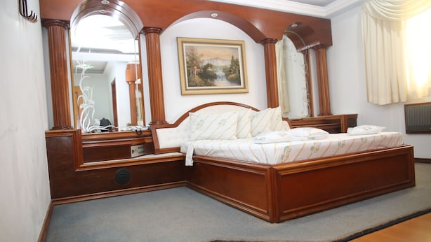 Un dormitorio con una cama de madera, un espejo grande y un cuadro en la pared.