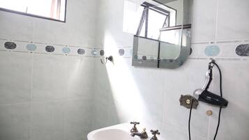 Un baño con un lavabo blanco, dos grifos, un espejo y un secador de pelo en la pared.