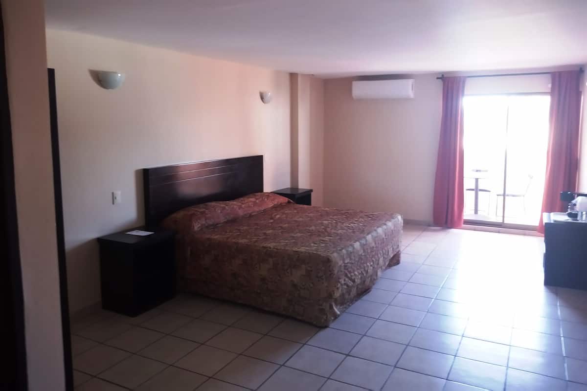 A hotel room with a bed, bedside tables, a window with curtains, and an air conditioning unit.