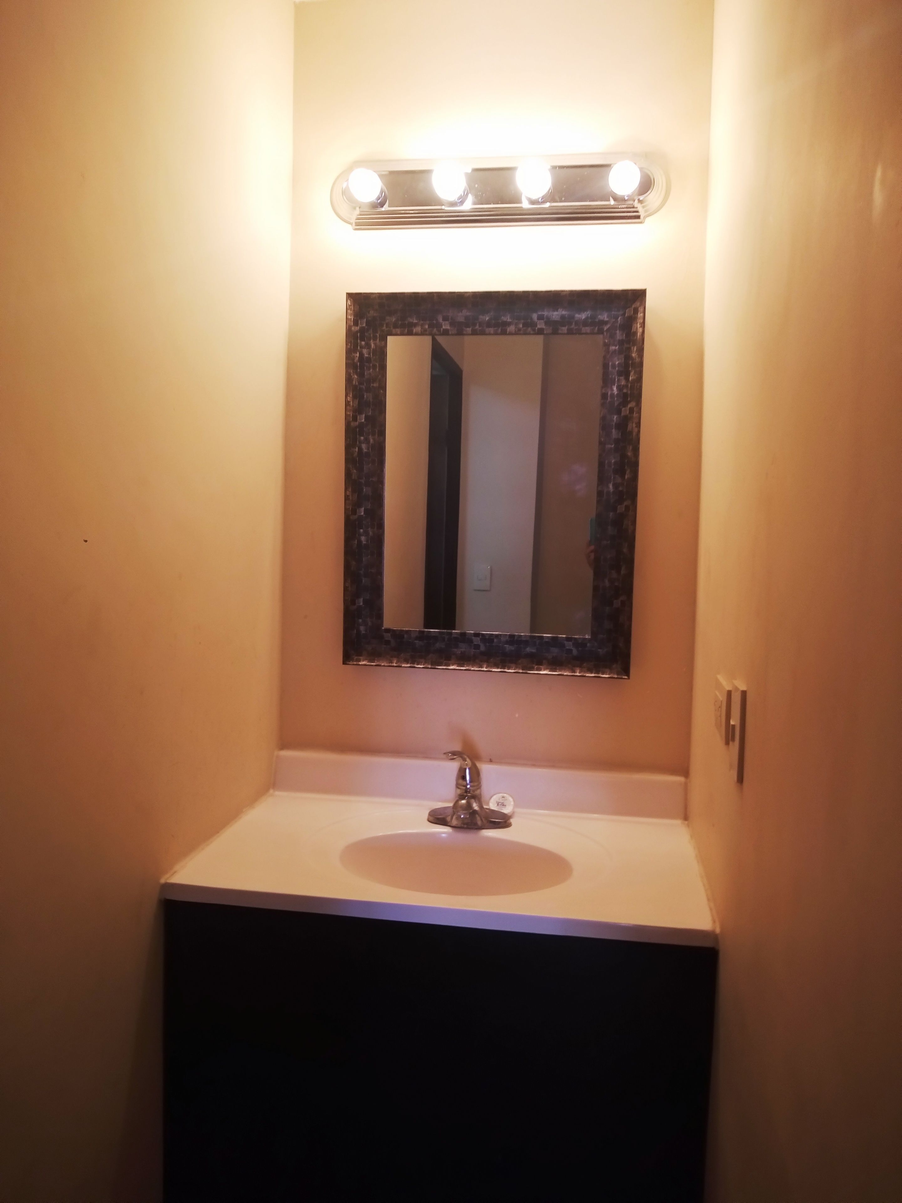Un bagno con un lavandino bianco, uno specchio con cornice nera e una luce sopra lo specchio.