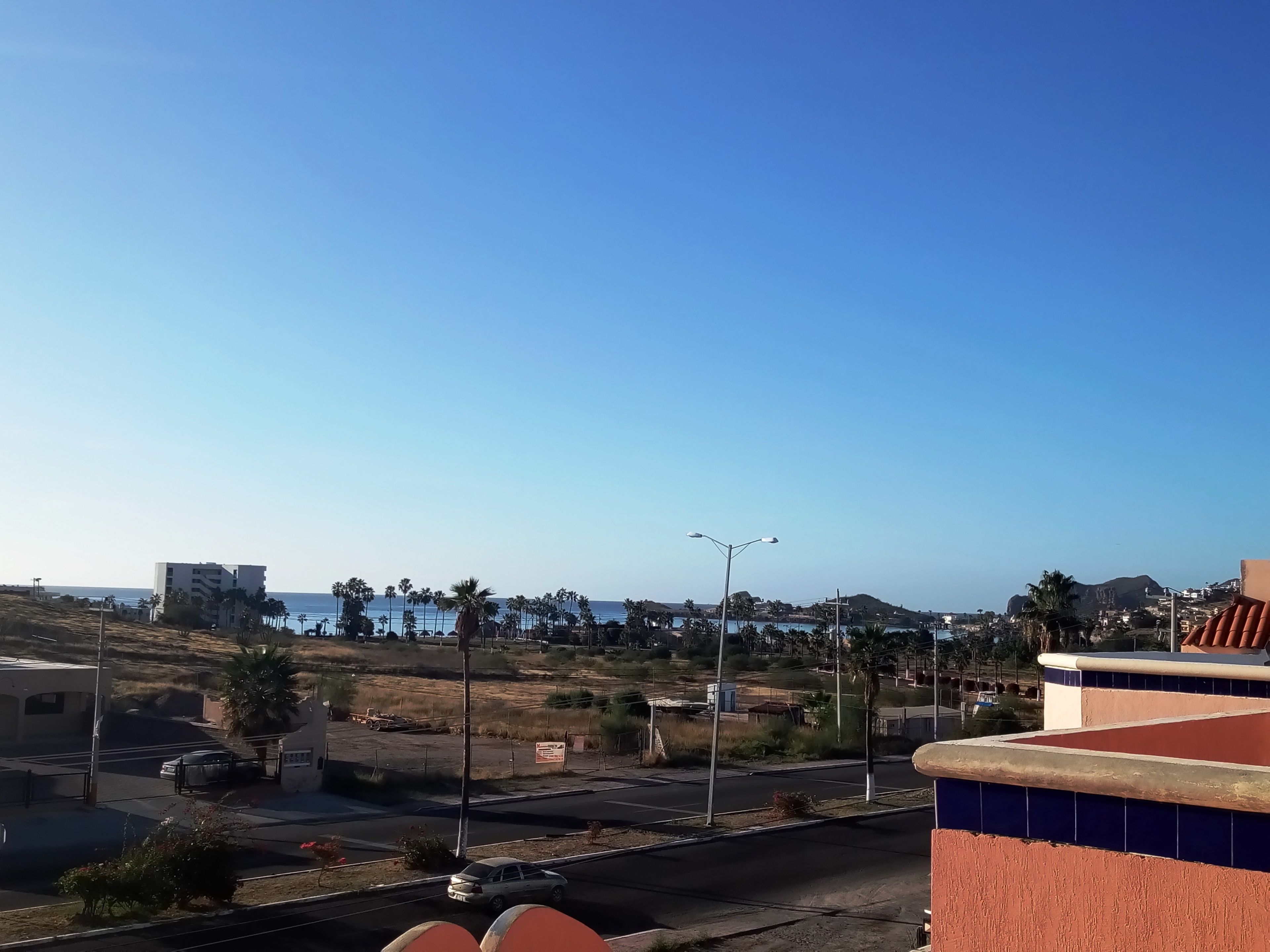 Un paisaje urbano costero con edificios, una carretera y cielo azul despejado.