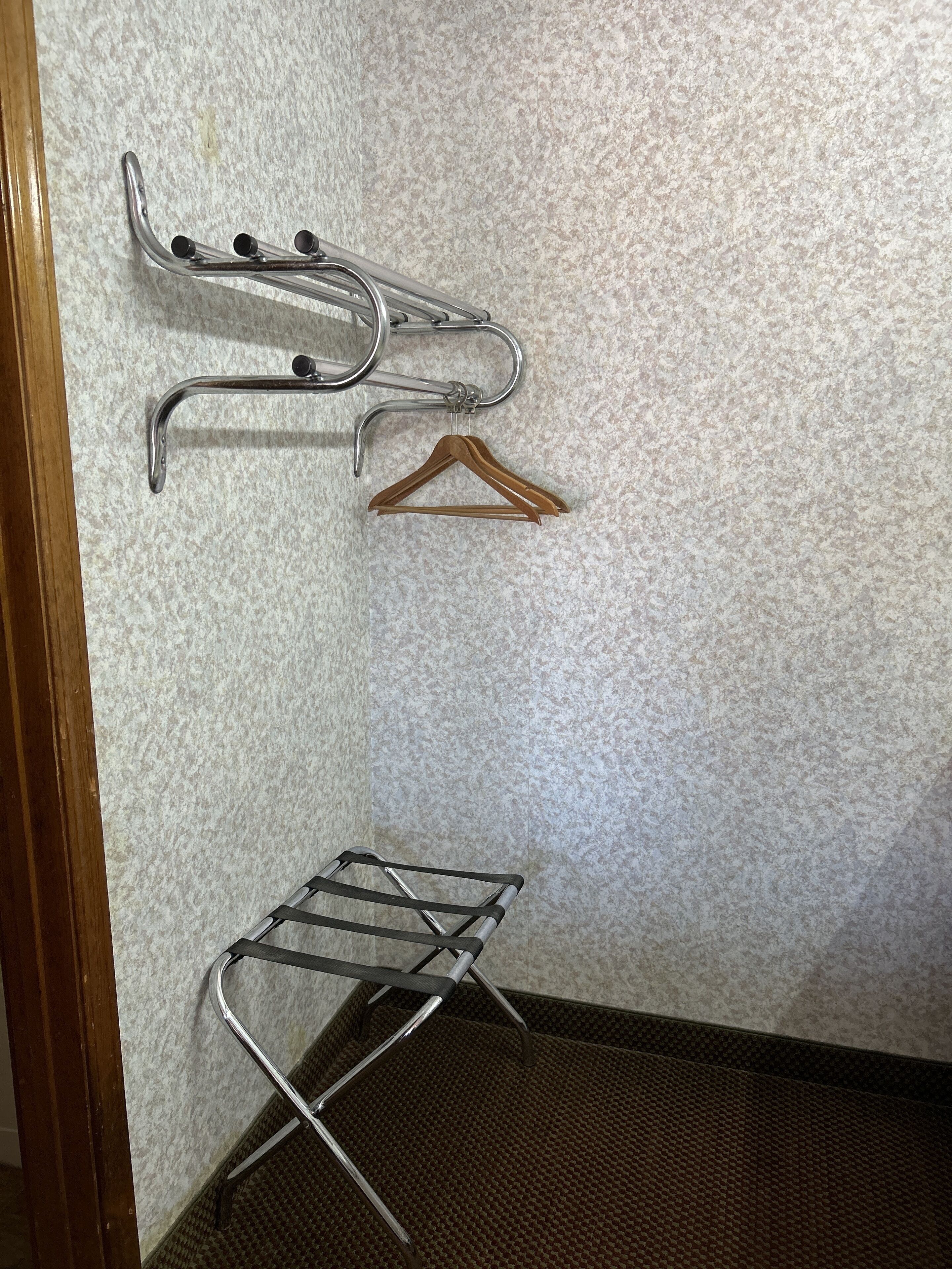 A corner of a room with a metal drying rack and a wooden hanger on a textured wall.