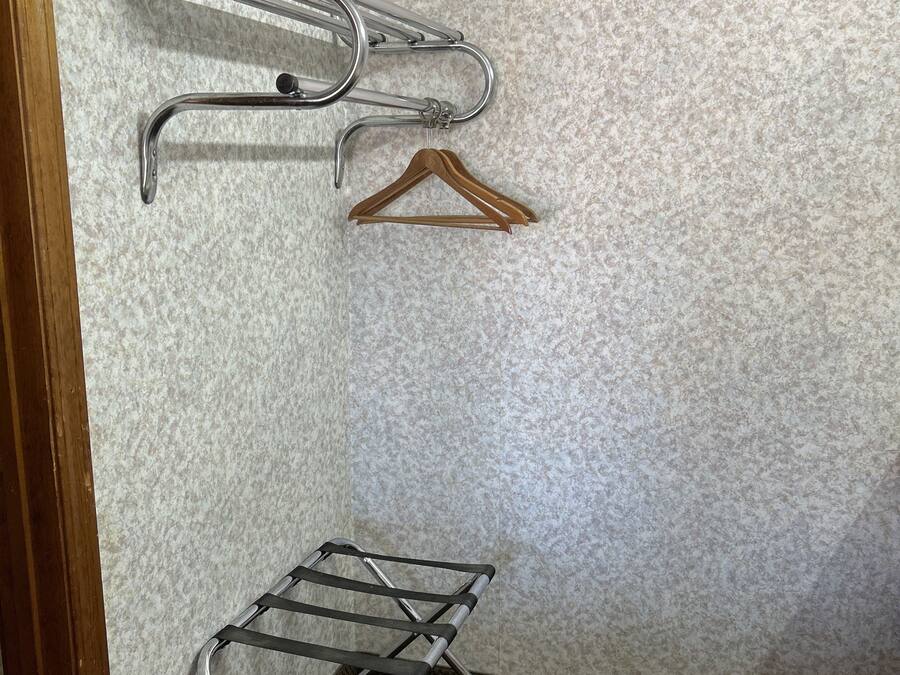 A corner of a room with a metal drying rack and a wooden hanger on a textured wall.