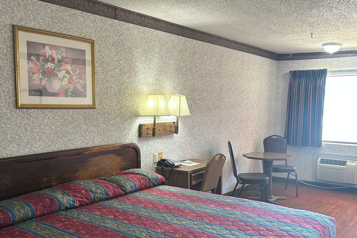 Habitación de hotel con una cama grande, un escritorio con silla, una lámpara y un cuadro en la pared.