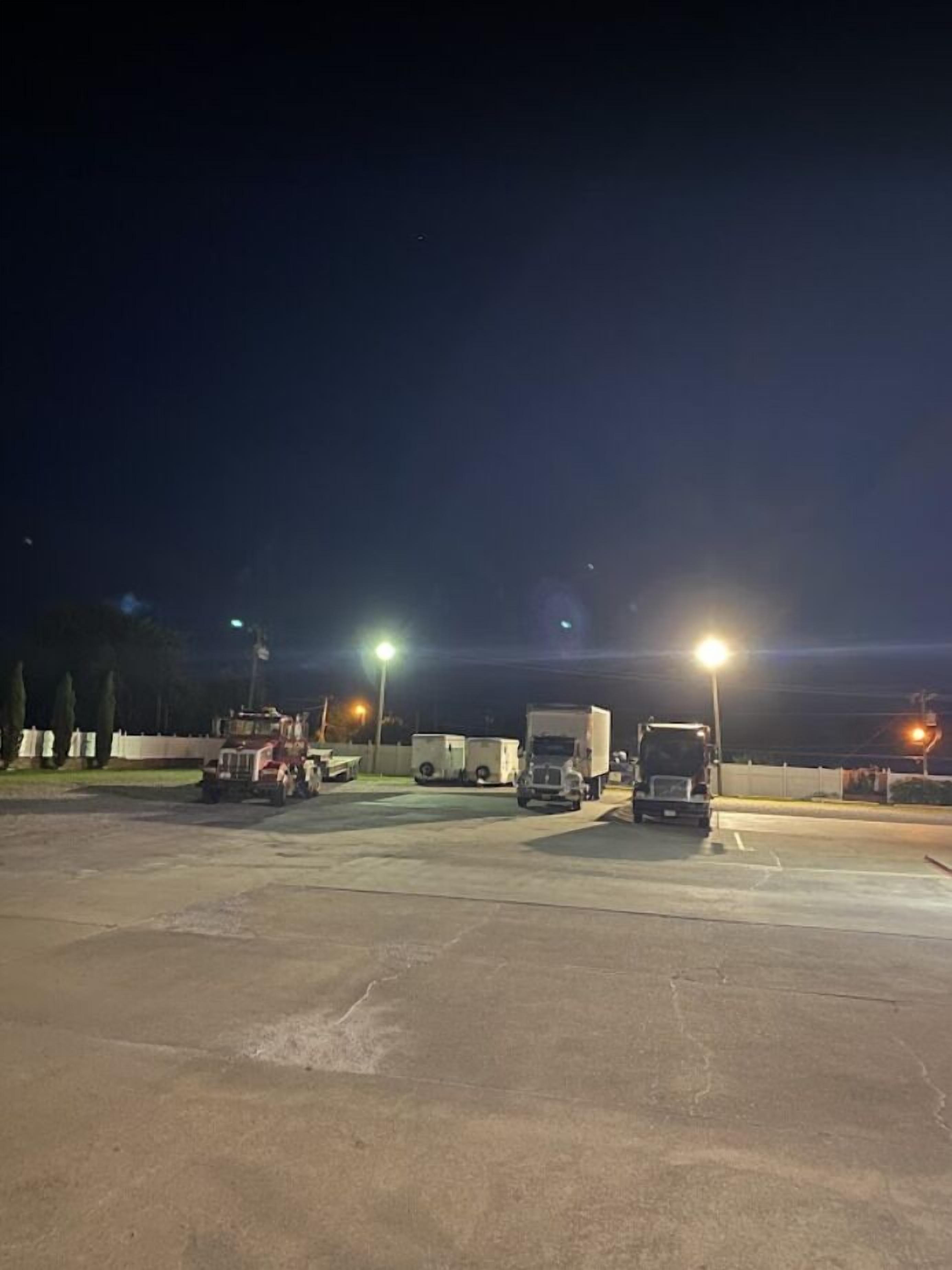 A parking lot at night with several trucks and a red vehicle.