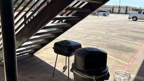 A parking area with a covered walkway, a barbecue grill, trash bins, and a water container. - Heritage Inn (Duncan)