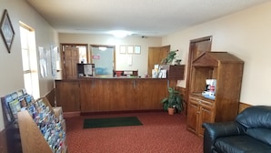 A reception area with a wooden counter, a green mat, a black leather couch, and a small potted plant. - Heritage Inn (Duncan)
