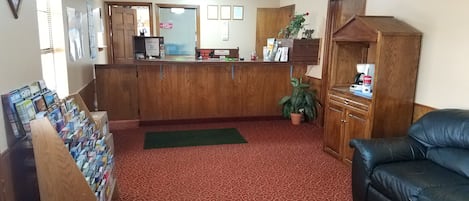 Una zona de recepció amb un taulell de fusta, un estora verd, un sofà de cuir negre i una petita planta en test.