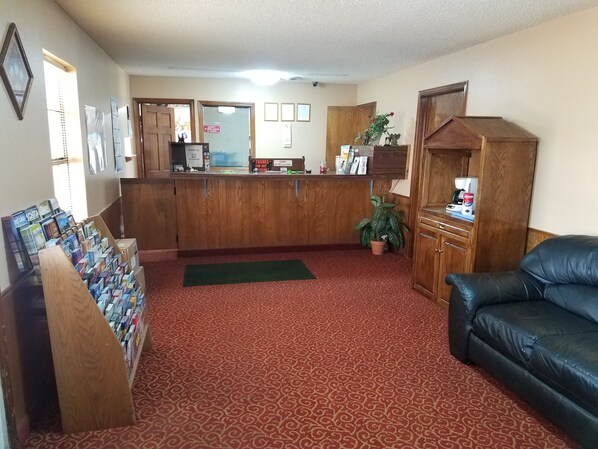 A reception area with a wooden counter, a green mat, a black leather couch, and a small potted plant.