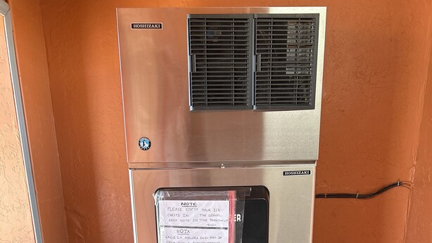 A commercial refrigerator with a water dispenser and a note requesting ice chest emptying. - Heritage Inn (Duncan)
