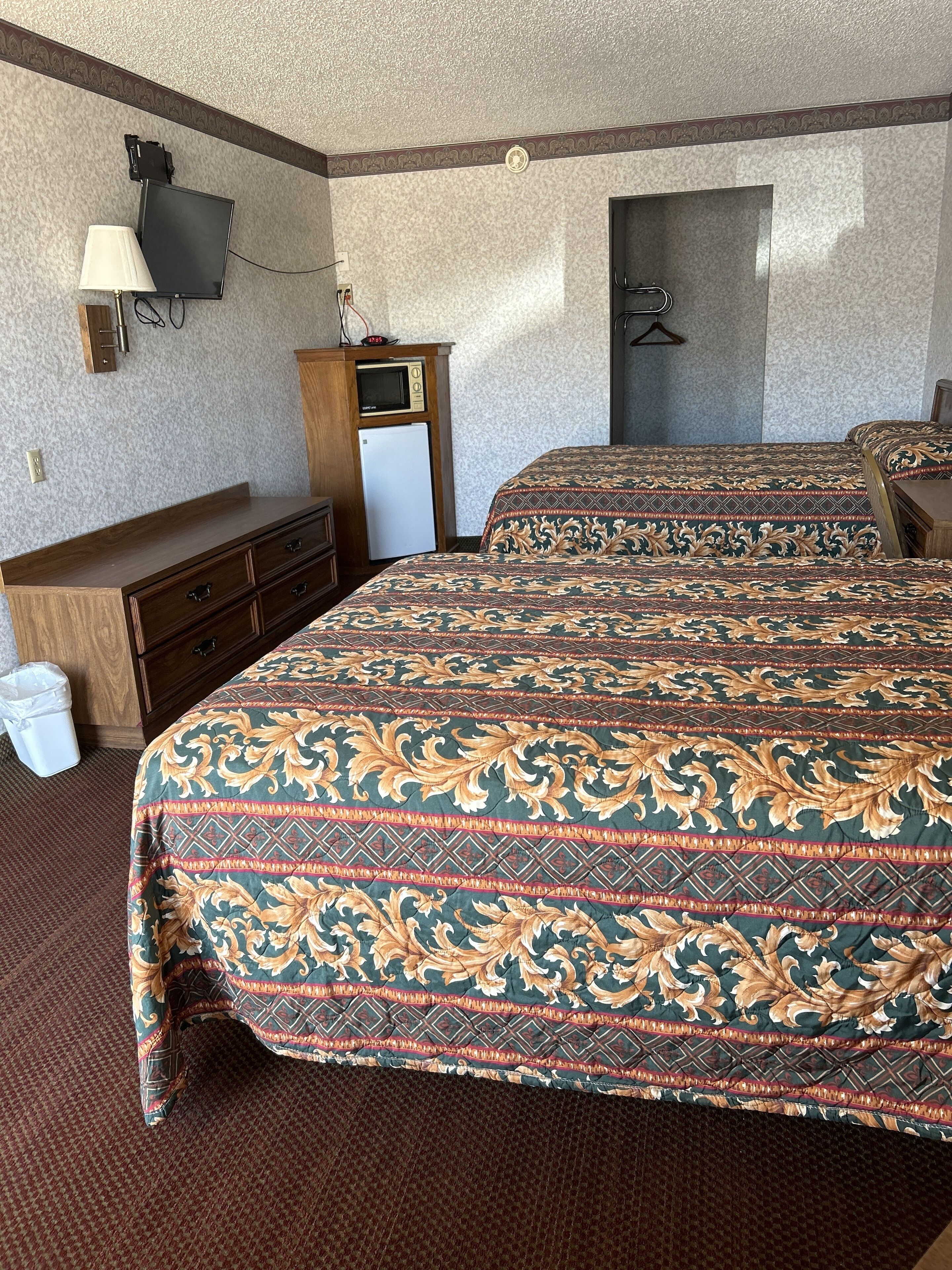 Ein Hotelzimmer mit zwei Betten, einem Schreibtisch, einer Mikrowelle und einem Fernseher.