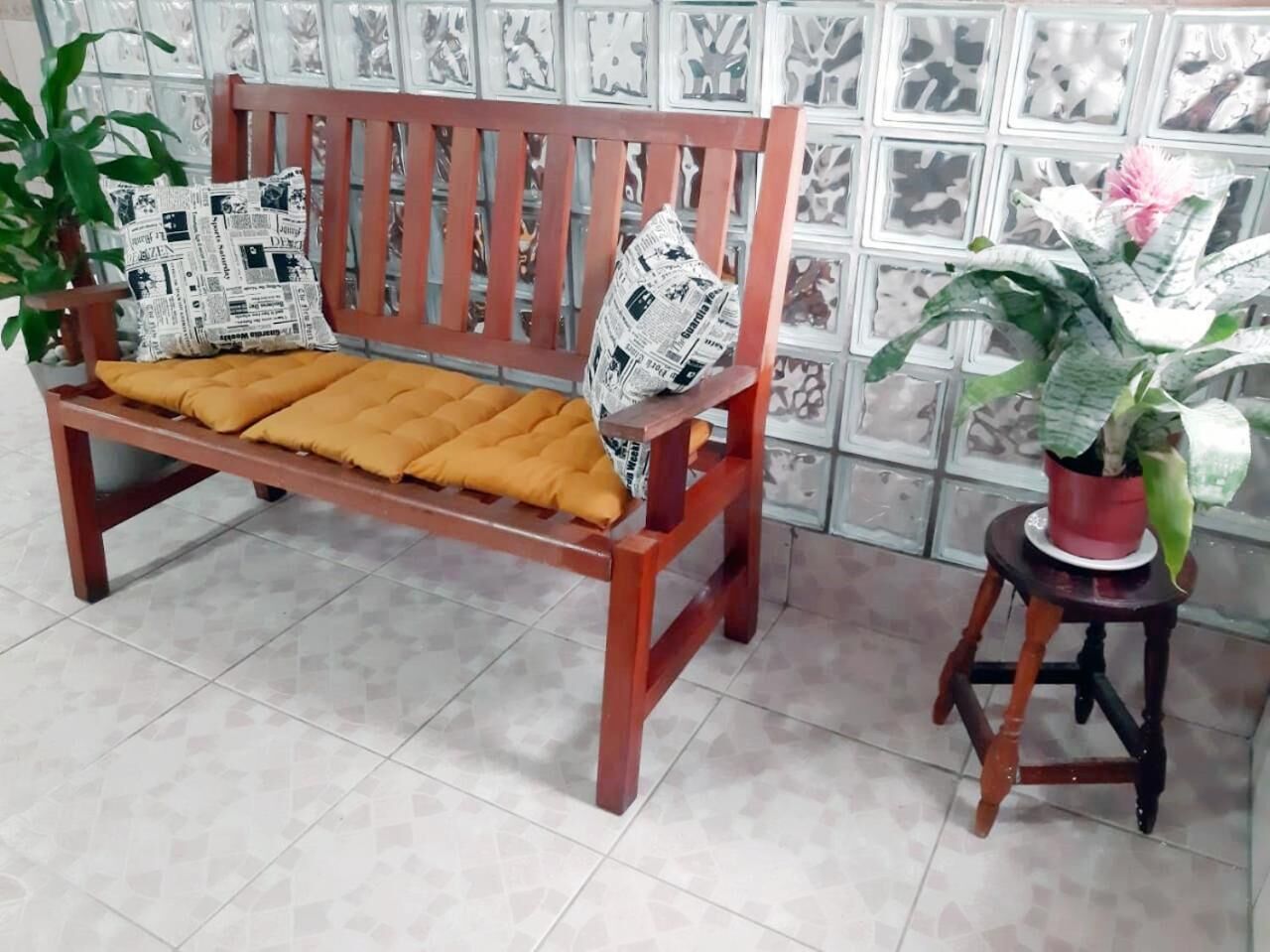 A wooden bench with yellow cushions and patterned pillows, a potted plant, and a tiled floor.